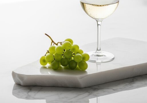 Cluster of fresh green grapes and sparkling white wine on a luxury marble surface.