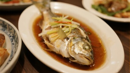 Steamed fish served with soy sauce, ginger, and scallions on a white oval plate