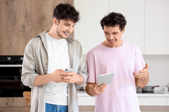 Young brothers using tablet computer and mobile phone in kitchen