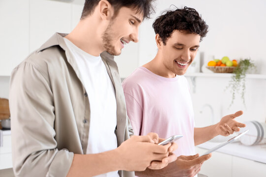 Young brothers using tablet computer and mobile phone in kitchen - Powered by Adobe