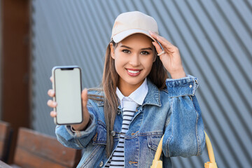 Young woman with blank mobile phone at table in street cafe