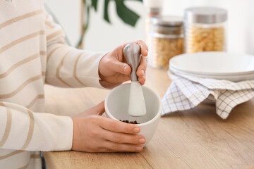 Woman grinding peppercorns in mortar on counter, closeup