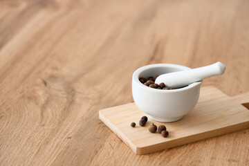 Ceramic mortar with pestle and peppercorns on wooden table, closeup