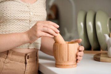 Woman with wooden mortar and pestle on counter in kitchen, closeup