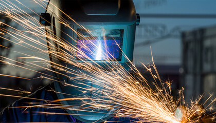 Industrial worker welding metal with bright sparks flying in factory workshop
