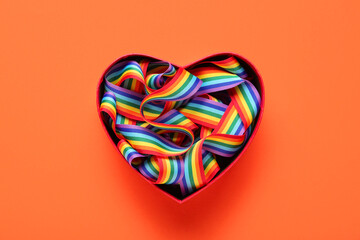 Heart-shaped gift box with rainbow ribbon on orange background. LGBT concept