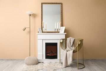 Fototapeta premium Interior of living room with armchair, lamp, mirror and candle holders on fireplace near beige wall