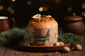 Tasty Christmas Panettone with fir branches, raisins and nuts on brown wooden table against blurred garland background