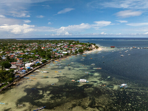 Wide aerial view of coastal town with sandy beach, pier, and boats anchored along shoreline. General Luna, Siargao, Philippines. - Powered by Adobe