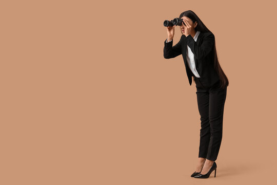 Young businesswoman looking through binoculars on beige background. Search concept - Powered by Adobe