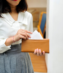 The body of a girl in a gray skirt and white shirt, her hand takes out a white paper from inside an elegant long brown leather wallet.