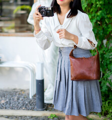 Girl's body in grey skirt and white shirt carrying beautiful tan leather bag while holding vintage camera