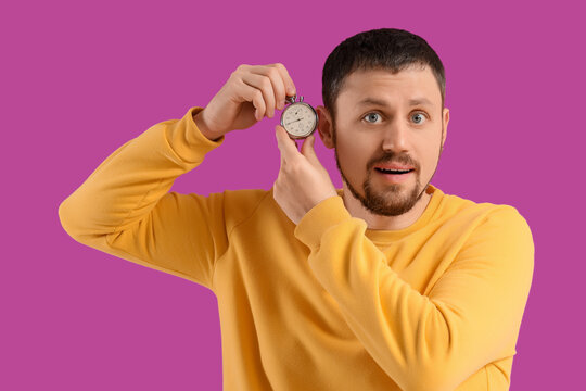 Young man with stopwatch on violet background