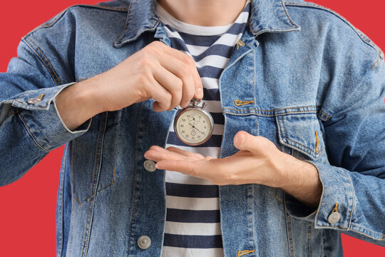Young man with stopwatch on red background, closeup