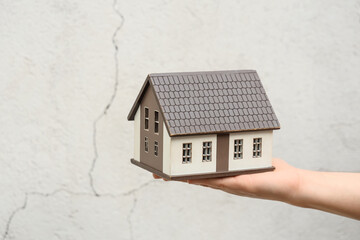 Female hand with house model against cracked wall. Earthquake concept