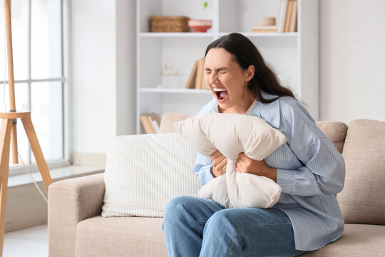 Screaming young woman with pillow sitting on sofa at home