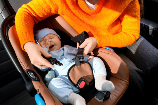 Young woman buckling her little baby in car seat