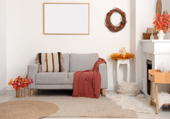 Fototapeta premium Comfortable sofa, fireplace and decor with autumn leaves in interior of living room