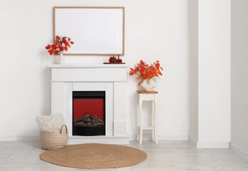 Fototapeta premium Fireplace, photo frame and vases with autumn leaves in interior of living room