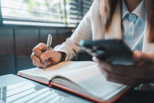 Professional woman multitasking with a smartphone and notebook, capturing a modern office work environment.