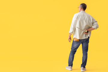Naklejka premium Mature man with tape measure on yellow background, back view