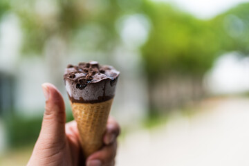 Hand holding chocolate ice cream in cone against nature background