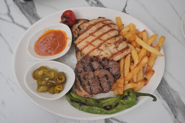 Grilled chicken and beef with fries on a white plate
