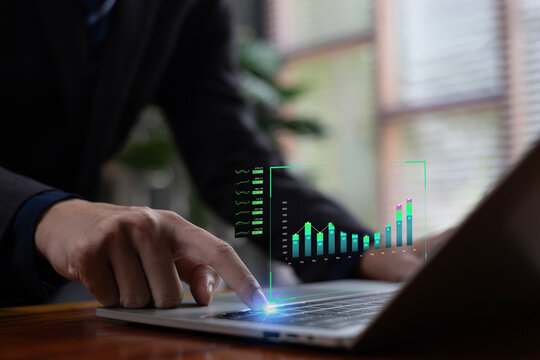 A business professional interacting with digital bar charts and financial metrics on a laptop, representing data analytics, financial growth insights, and modern business intelligence technology. - Powered by Adobe