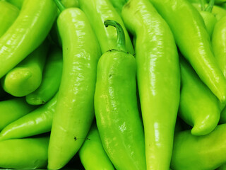 Close-up view of fresh green chili peppers piled together, showcasing their smooth texture and vibrant color. Ideal for themes related to organic produce, spicy vegetables, farming, and food markets.