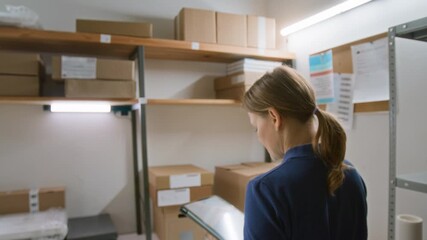 Medium follow shot of young Caucasian woman walking in office of express delivery company along racks, scanning barcodes on packages then typing on tablet computer while tracking parcels
