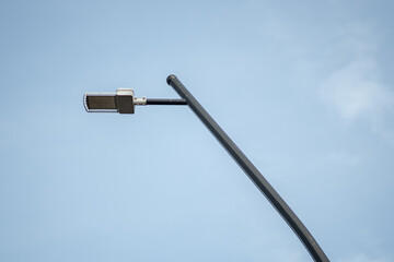 Minimalist modern LED street lamp post isolated against a clear bright blue sky background.