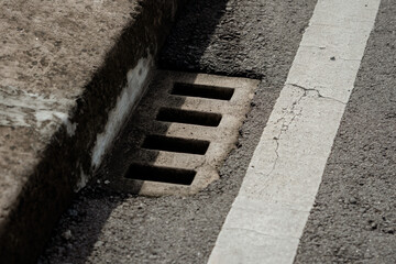 Concrete drainage grate on an asphalt road side next to a white painted traffic line markings.