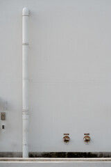 Vertical white drainage pipe on a textured white wall with two brass fire hose valves at the bottom.