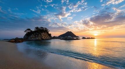 A beautiful sunset casts vibrant colors over waves gently lapping a sandy beach. Rocks rise from the water, framed by a peaceful landscape and dramatic clouds.