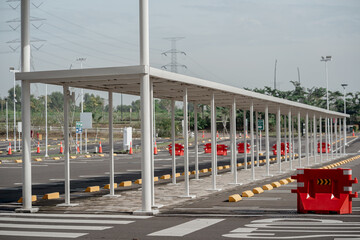 Long white metal parking shelter canopy with red barriers in an empty outdoor asphalt car park area.
