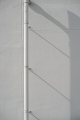 Vertical white drainage pipe casting a long diagonal shadow on a textured gray concrete wall surface.