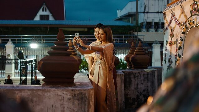 Thai women in traditional dress taking selfie at wat arun during festival - Powered by Adobe