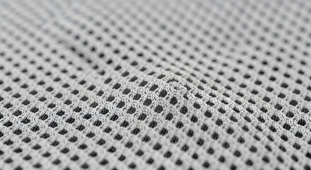 Close up view of a light grey mesh fabric with a repeating diamond pattern and a dark background