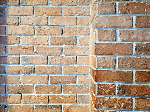 Close up of an old, weathered orange brick wall corner with rough texture and white mortar.