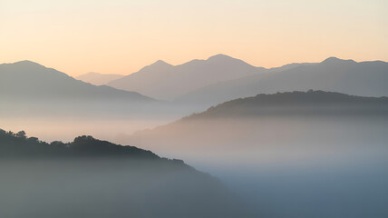 Obraz premium Fog blankets hilly mountainsides during a muted, dreamlike sunrise with gentle light in the distance