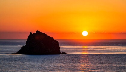 Spectacular sunset over the ocean with a rocky island silhouette.