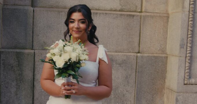 A beautiful brunette bride walks with a bouquet and looks into the camera.