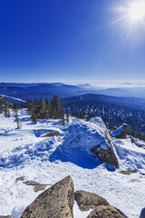 Panoramic view of mountain ridges in fog and sky in Sheregesh, Russia. Beauty white blue peaks Altay mountains fades in distance. Snow conifer forest and stones at bright winter sun on mount Ytuya.
