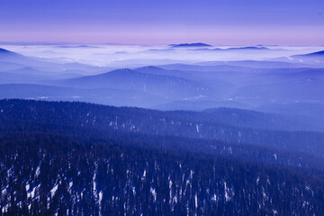 Panoramic view of mountain ridges covered morning mist and  blue pink pastel colored sky. Distant peaks fade smoothly in horizon, creating depth effect under clear winter sky. Scenic landscape.