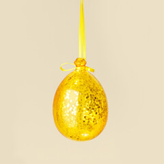 Christmas decoration sparkling golden ball hanging on yellow ribbon on beige background, minimal New Year trend. Xmas seasonal yellow bauble side view as stylish holidays monochrome card, copyspace
