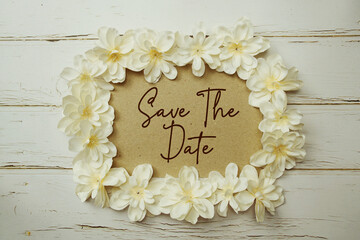 Save The Date text written on paper card with flower decoration on wooden background