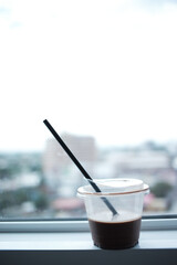 Refreshing brown coffee drink in transparent plastic cup with black straw. Quietly resting against bright window, it evokes serene and peaceful moment, ideal for contemplation