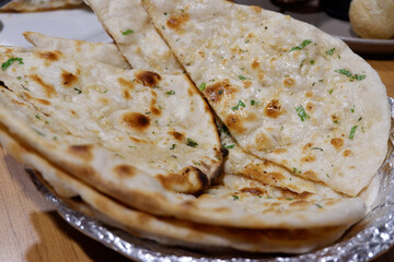 Freshly baked garlic naan bread, delightful Indian food, brings wonderful aromatic experience. Fluffy flatbread, golden brown with green herbs, offers comforting and satisfying culinary joy