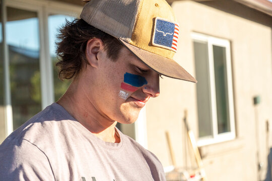 A man in a hat and tshirt has a flag painted on his face