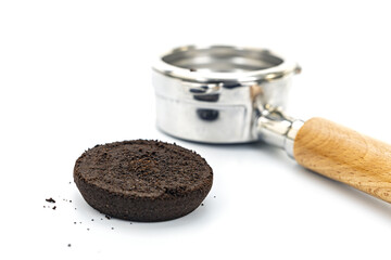 Close-up of used compacted coffee grounds next to a metal portafilter with wooden handle on white background
